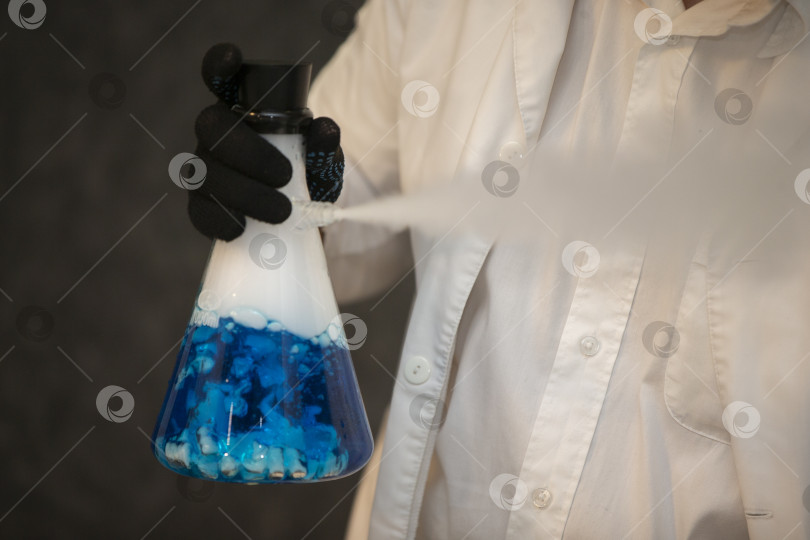 Скачать Химическая колба с синим раствором в руках лаборанта. Опыты и эксперименты. фотосток Ozero