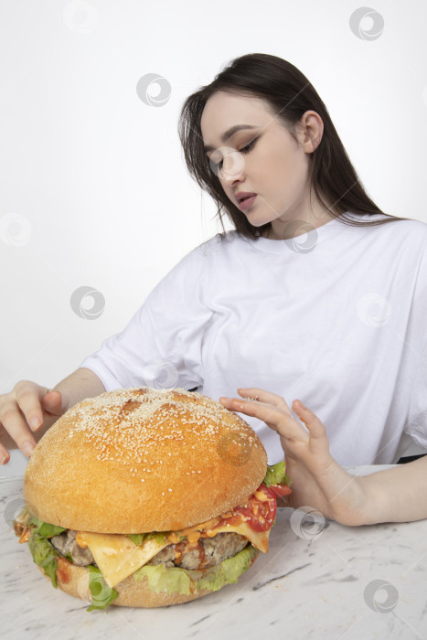Скачать На заднем плане женщина держит большой бутерброд с гамбургером барбекю. Концепция фаст-фуда. У девушки огромный гамбургер. фотосток Ozero