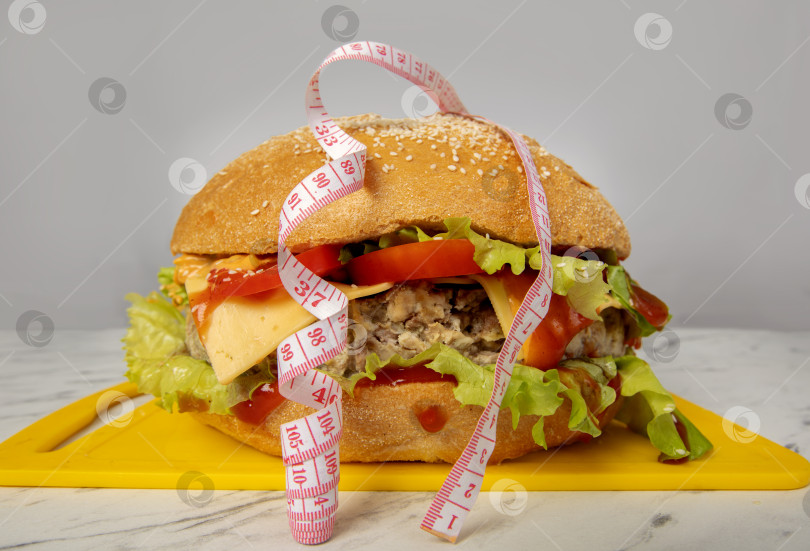 Скачать Гамбургер, обернутый рулеткой, на сером фоне. Концепция похудения. фотосток Ozero