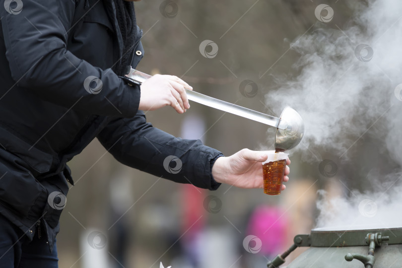 Скачать Чайный мастер разливает чай в пластиковый стакан на открытом воздухе. фотосток Ozero