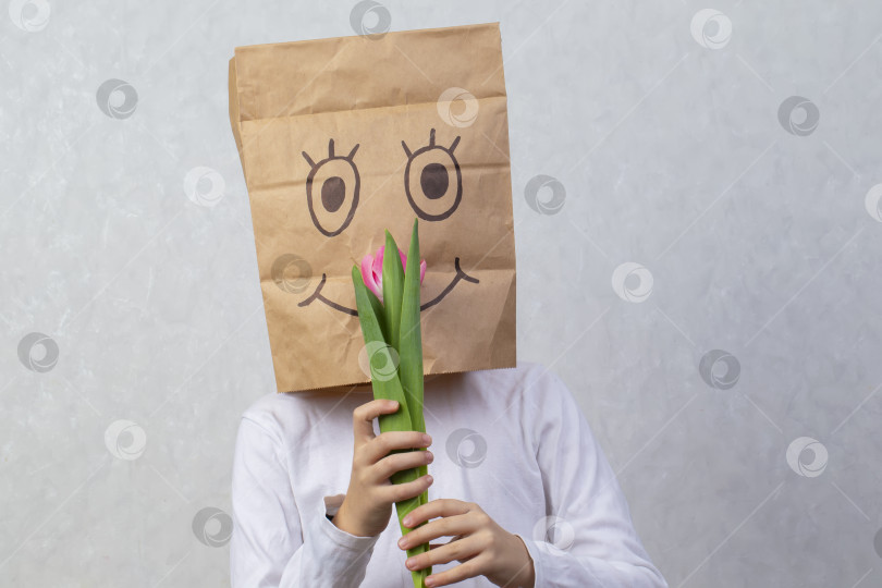 Скачать Ребенок с картонной коробкой на голове держит тюльпан. Концепция анонимного подарка. фотосток Ozero