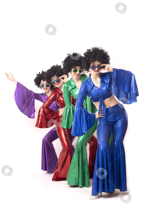 Скачать Группа девушек в ярких расклешенных костюмах и африканских париках позирует на белом фоне. Стиль диско восьмидесятых или семидесятых годов. фотосток Ozero