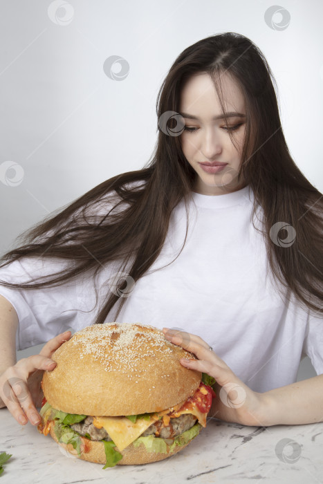 Скачать На заднем плане женщина держит большой бутерброд с гамбургером барбекю. Концепция фаст-фуда. У девушки огромный гамбургер. фотосток Ozero