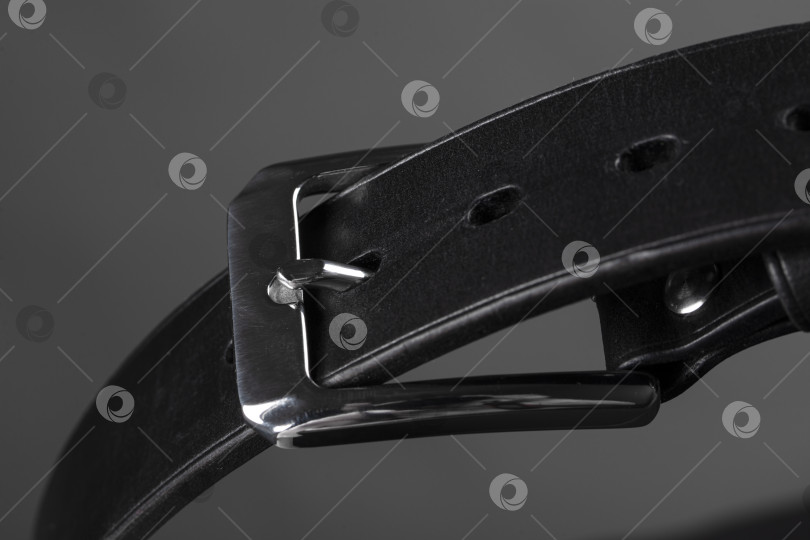 Скачать Фрагмент черного кожаного ремня с металлической пряжкой крупным планом на сером фоне. фотосток Ozero