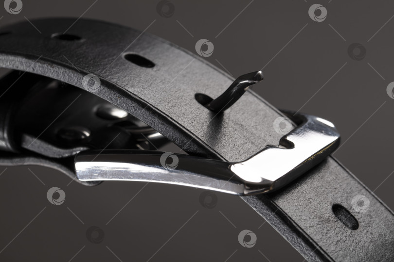 Скачать Фрагмент черного кожаного ремня с металлической пряжкой крупным планом на сером фоне. фотосток Ozero