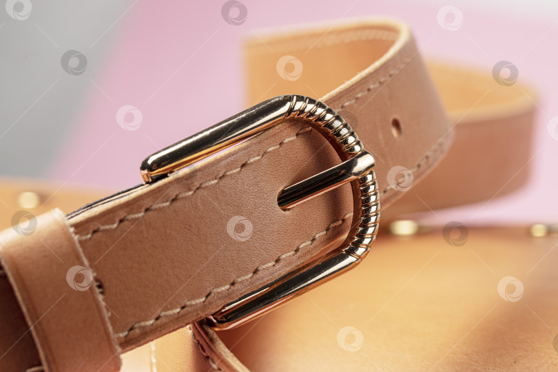 Скачать Деталь дорогого изделия из коричневой кожи со строчкой и металлической пряжкой на розовом фоне. фотосток Ozero