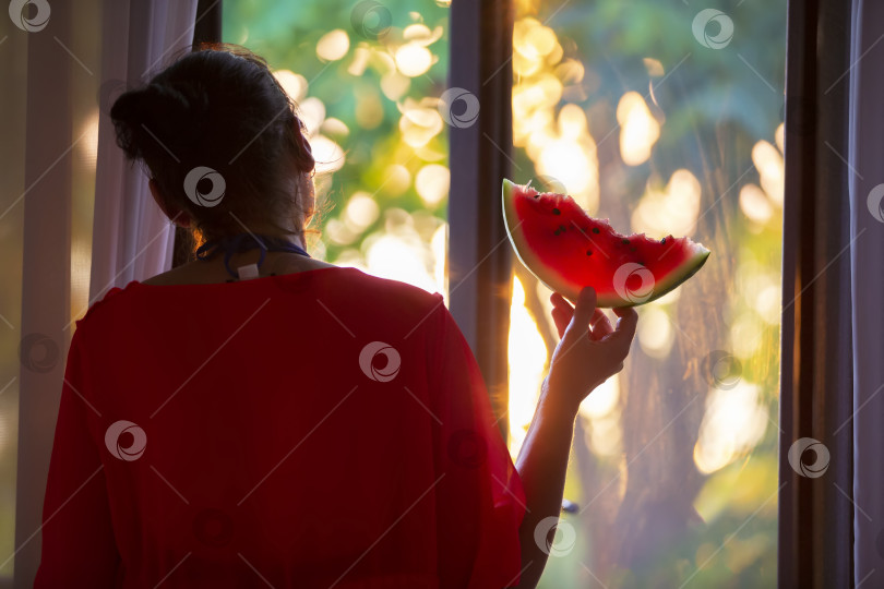 Скачать Силуэт женщины у окна с арбузом в лучах заходящего солнца. фотосток Ozero