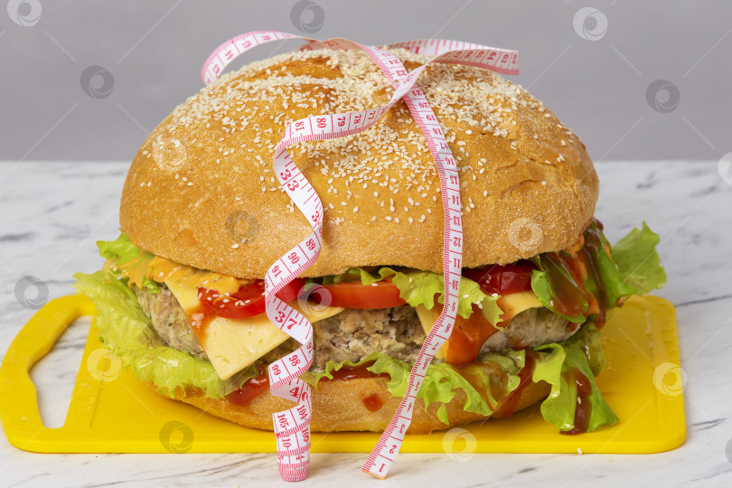 Скачать Гамбургер, обернутый рулеткой, на сером фоне. Концепция похудения. фотосток Ozero