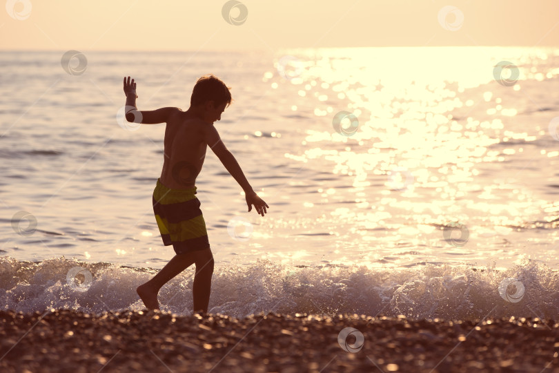 Скачать Силуэт мальчика у моря на закате. Он бежит по берегу, играет с волной. фотосток Ozero