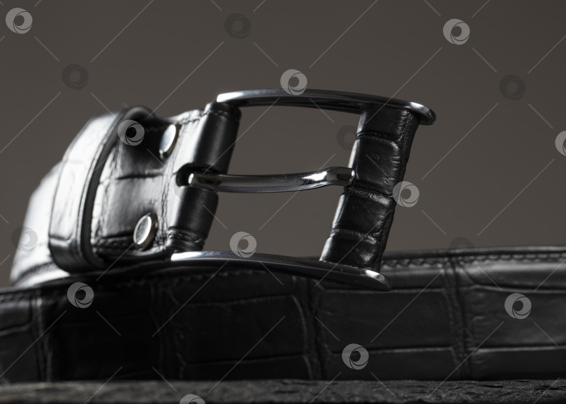 Скачать Черный кожаный ремень с металлической бляхой крупным планом на сером фоне. фотосток Ozero