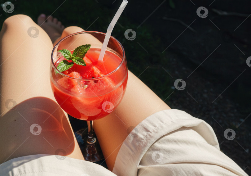 Скачать Женщина, отдыхающая на свежем воздухе с освежающим напитком из арбуза. Летняя концепция освежения и релаксации, идеально подходящая для отпуска. фотосток Ozero