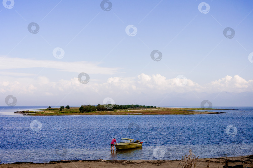 Скачать Иркутск, Россия, 2 мая 2018 года, Мужчина-рыбак сталкивает старую ржавую лодку в воду озера Байкал, летний пейзаж фотосток Ozero