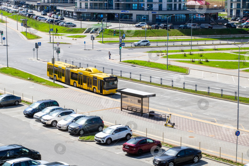 Скачать Беларусь, Минск - 01.05.2025: Желтый автобус проезжает по оживленной улице рядом с парковкой для автомобилей фотосток Ozero