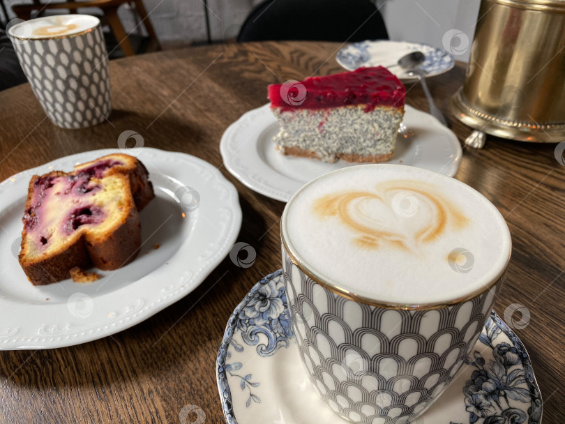 Скачать Кофе с пенкой "сердечко" и десерты на деревянном столе с пирожными в уютной обстановке кафе фотосток Ozero