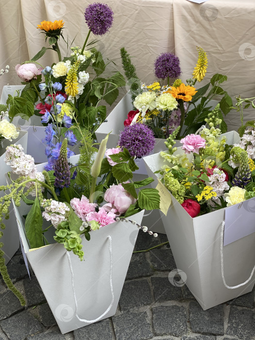 Скачать Букет ярких цветов в белых подарочных пакетах на каменной мостовой, идеально подходящий для весенних мероприятий фотосток Ozero