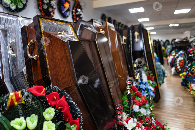 Скачать Внутри магазина ритуальных услуг находятся деревянные гробы и венки из сверкающих цветов фотосток Ozero