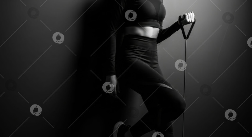 Скачать Женщина в спортивной одежде, держащая в руках резинку сопротивления, выделена на темном фоне. фотосток Ozero