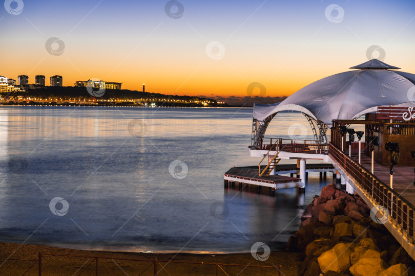Скачать город Геленджик, Краснодарский край, Россия, 7 ноября 2024 года. Закат на пляже курорта Геленджик. Красивый пляж с пирсом и большой палаткой фотосток Ozero