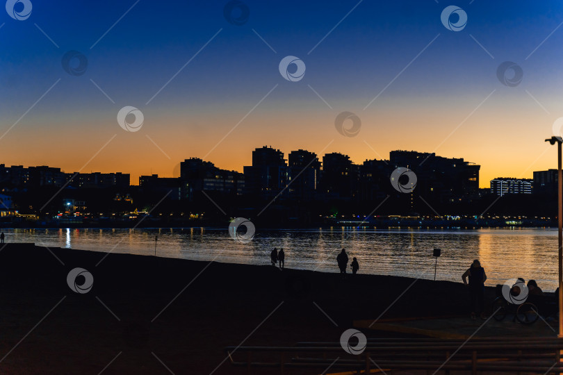 Скачать город Геленджик, Краснодарский край, Россия, 7 ноября 2024 года. Закат на пляже курорта Геленджик. Группа людей сидит на скамейках у воды, любуясь закатом фотосток Ozero