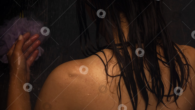 Скачать Женщина принимает душ, держа в руке губку фотосток Ozero