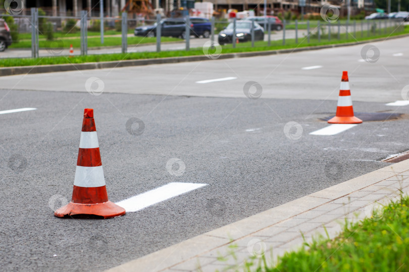 Скачать Два дорожных конуса, оранжевый и белый, расположены на обочине дороги фотосток Ozero