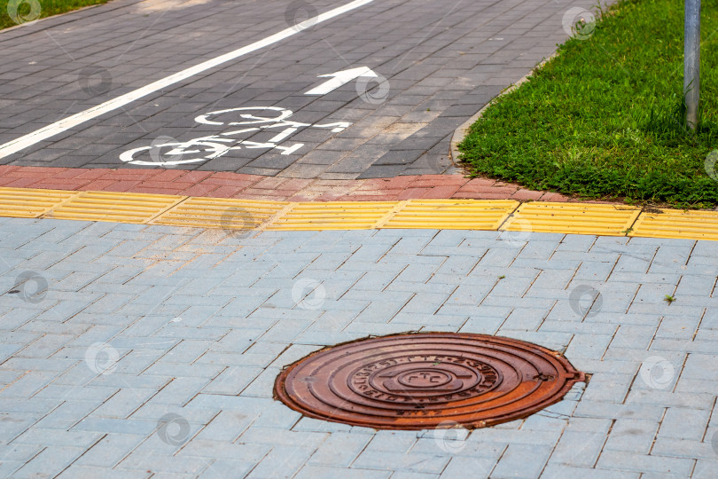 Скачать На тротуаре рядом с велосипедной дорожкой установлена крышка канализационного люка фотосток Ozero