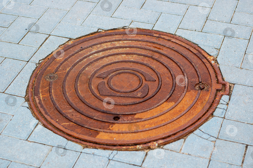 Скачать На кирпичном тротуаре стоит ржавая крышка канализационного люка фотосток Ozero
