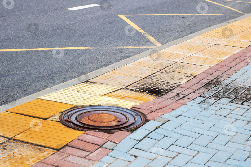 Скачать На тротуаре рядом с дорогой установлена круглая крышка канализационного люка фотосток Ozero
