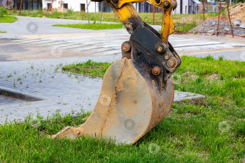 Скачать Ярко-желтый ковш экскаватора покоится на зеленой траве фотосток Ozero