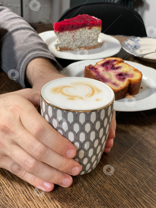 Скачать Человек, держащий кофейную чашку с рисунком латте, десерт на заднем плане на деревянном столе фотосток Ozero