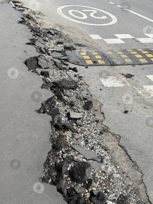 Скачать Поврежденная городская дорога с выбоинами возле пешеходного перехода и лежачим полицейским в городе фотосток Ozero