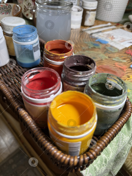 Скачать Художественные принадлежности в баночках с яркими красками разложены в корзине на текстурированном фоне фотосток Ozero
