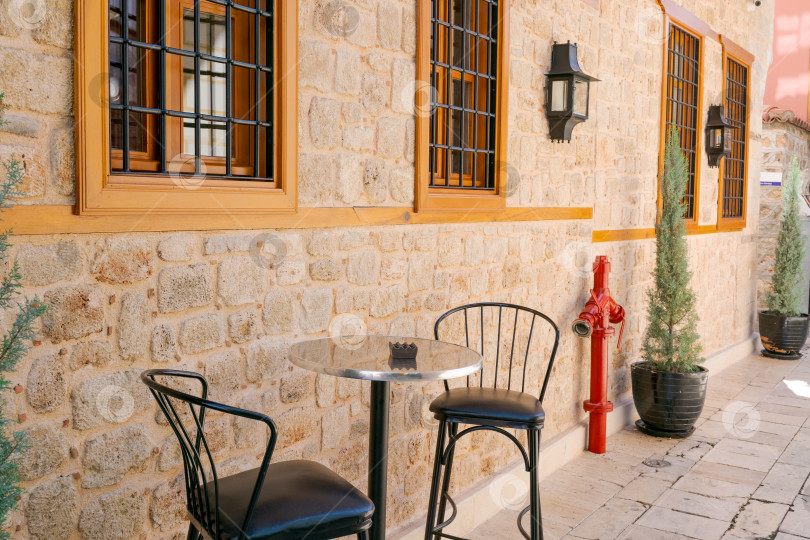 Скачать Красный пожарный гидрант стоит на тротуаре рядом со столом и двумя стульями фотосток Ozero