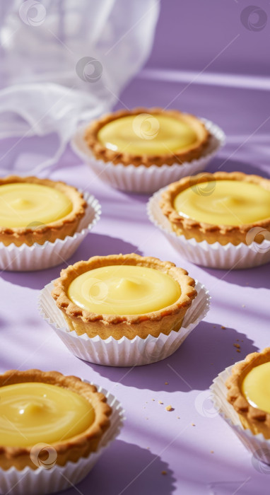 Скачать Множество сладких лимонно-творожных тарталеток в белых бумажных стаканчиках на фиолетовом фоне. Десертно-закусочное хлебобулочное изделие для вечеринки или кафе. фотосток Ozero