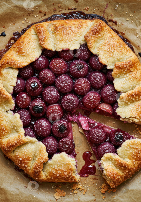 Скачать Вид сверху на вкусный домашний ягодный галет или деревенский пирог с пропущенным кусочком, испеченный на пергаментной бумаге на десерт. фотосток Ozero