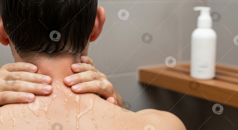 Скачать Мужчина принимает душ и прикасается сзади к своей мокрой шее и плечу. Мужская гигиена и ежедневный уход за собой. Флакон косметического средства. фотосток Ozero