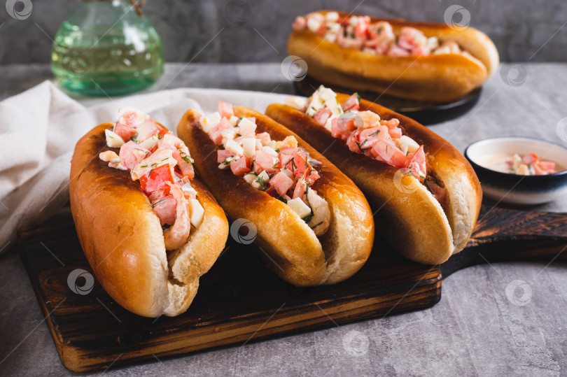 Скачать Вкусные хот-доги в обжаренных булочках с салатом из помидоров, яиц и креветок на доске фотосток Ozero