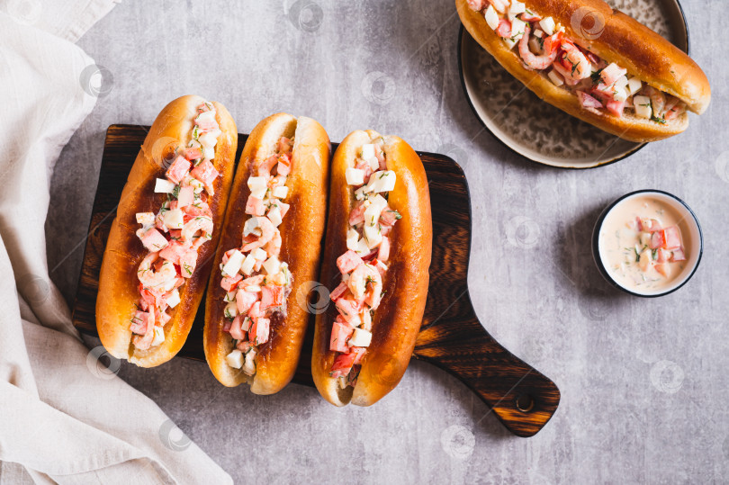 Скачать Вкусные хот-доги в обжаренных булочках с салатом из помидоров, яиц и креветок на доске, вид сверху фотосток Ozero
