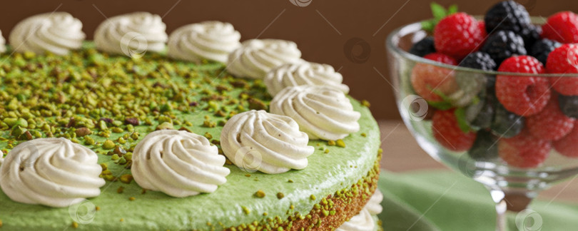 Скачать Вкусный фисташковый торт, украшенный завитками из безе и измельченными орехами, со свежими ягодами в стеклянном бокале - концепция десерта. фотосток Ozero
