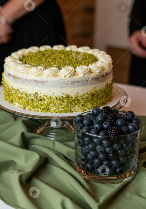 Скачать Вкусный слоеный фисташковый торт на стеклянной подставке со свежей черникой в бокале, готовый к десертному столу. фотосток Ozero