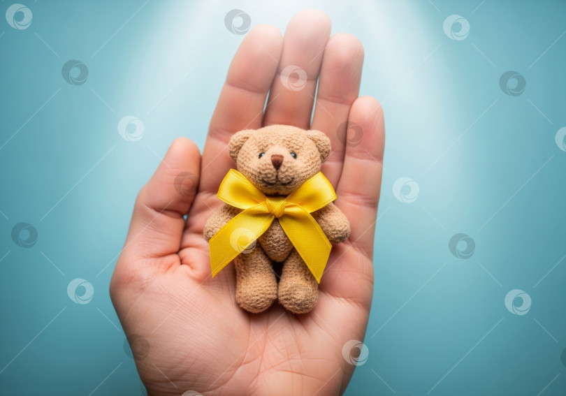 Скачать Маленький плюшевый мишка с желтой лентой в одной руке на синем фоне фотосток Ozero