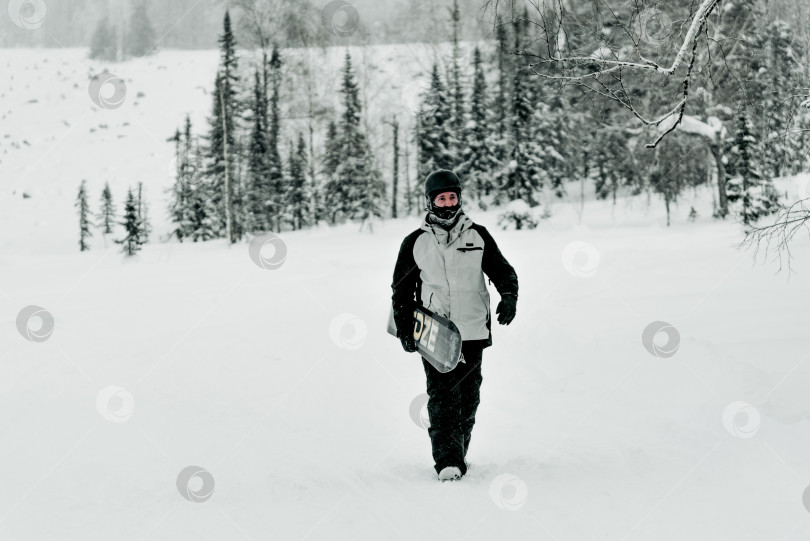 Скачать Шерегеш, Россия, 4 января 2021 года, Сноубордист-лыжник идет пешком и держит в руках сноуборд фотосток Ozero