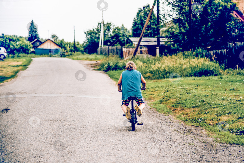 Скачать Белокуриха, Россия, 28 июня 2017 года, Девушка едет на велосипеде по разбитой дороге в деревне фотосток Ozero