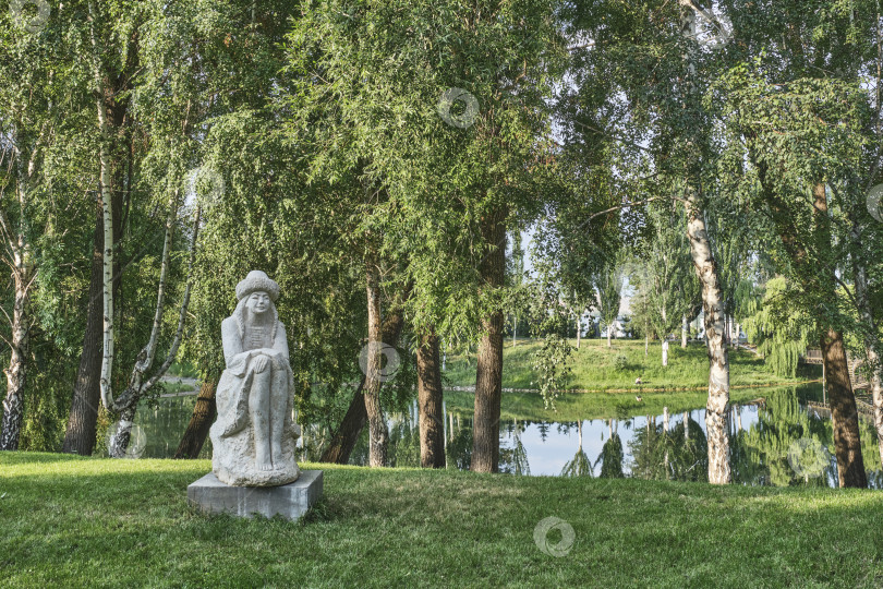 Скачать Скульптура киргизской девушки Мырзагуль, сидящей на камне на лужайке в парке фотосток Ozero