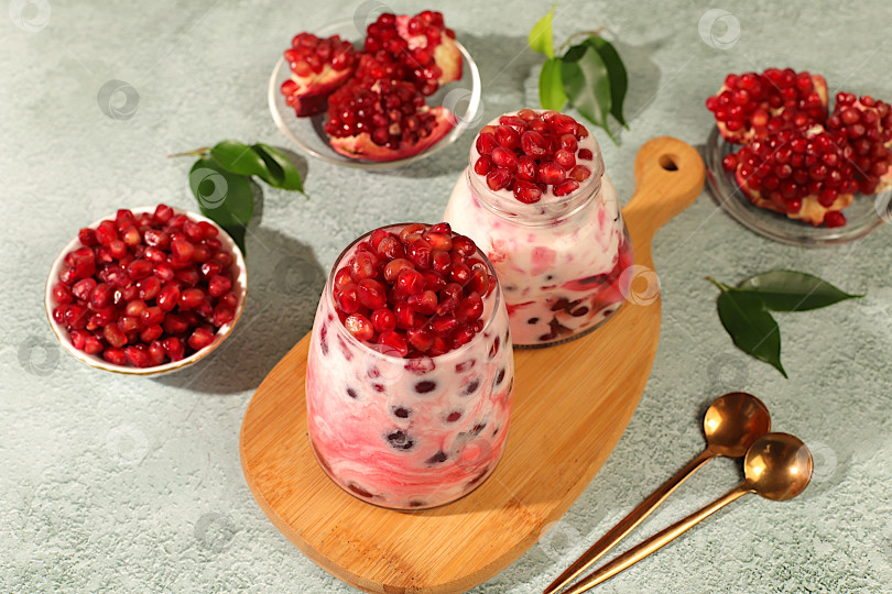 Скачать Бокалы с гранатовым йогуртом с кусочками граната, изюмом и свежими сливками для здорового питания. Полезный завтрак с ингредиентами, история кухни, концепция натурального питания и диеты, меню для кафе, ресторана. фотосток Ozero