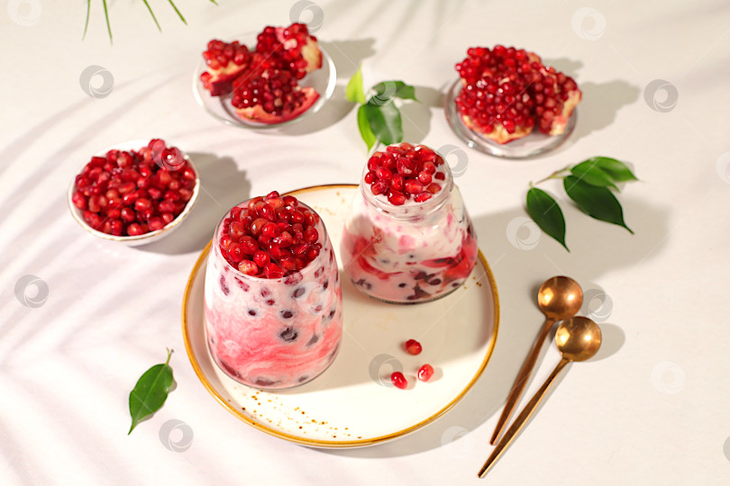 Скачать Бокалы с гранатовым йогуртом с кусочками граната, изюмом и свежими сливками для здорового питания. Полезный завтрак с ингредиентами, история кухни, концепция натурального питания и диеты, меню для кафе, ресторана фотосток Ozero