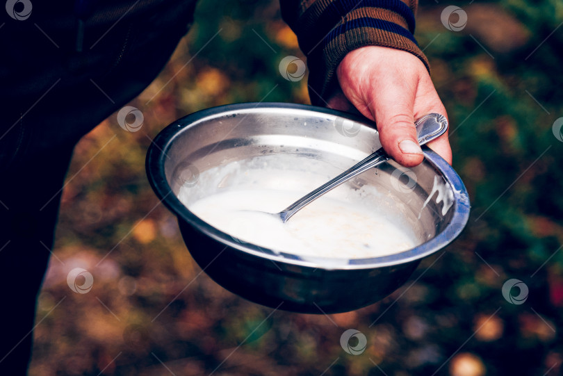 Скачать Турист готовит походную еду для пикника на кухне у костра, мужчина держит металлическую тарелку фотосток Ozero