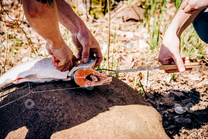 Скачать Турист готовит походную еду для пикника на кухне у костра, мужчина режет красную рыбу фотосток Ozero