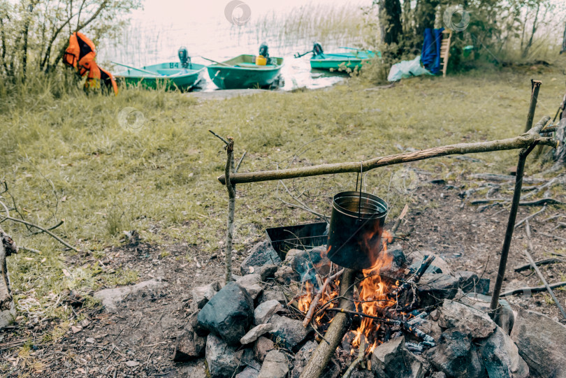 Скачать Турист готовит походную еду для пикника на кухне у костра, подвешивает котел над огнем фотосток Ozero