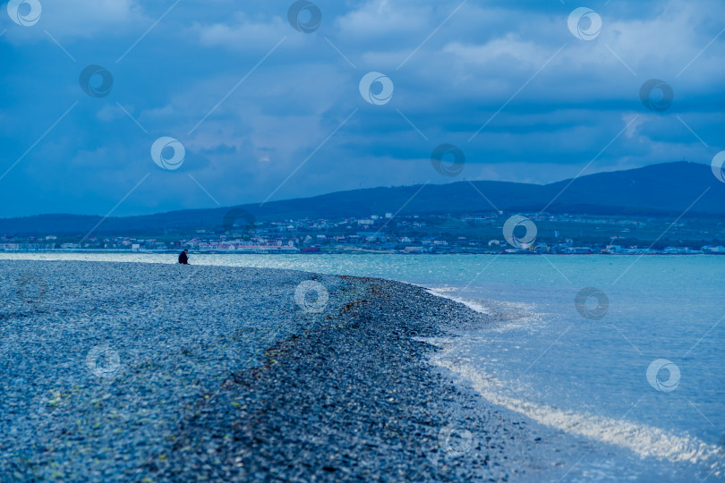 Скачать Курорт Геленджик. В вечерних сумерках мужчина сидит в одиночестве на берегу Геленджикской бухты. Кавказские горы на горизонте фотосток Ozero